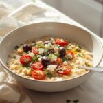 A vibrant Mediterranean savory oatmeal main dish topped with roasted tomatoes, feta, olives, and fresh herbs.