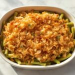 Golden, crispy Air Fryer Green Bean Casserole in a ceramic baking dish, garnished with thyme on a light marble surface.