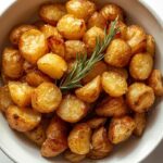 A beautiful bowl of golden-brown, perfectly crispy roasted potatoes garnished with fresh rosemary and sea salt, ready to serve.