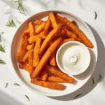 A plate of perfectly golden crispy baked sweet potato fries with a dipping sauce, a delicious and healthy sweet potato side for kids.