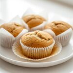 Close-up of three perfect gluten-free muffins on a white plate, showcasing golden tops and a light, airy crumb.